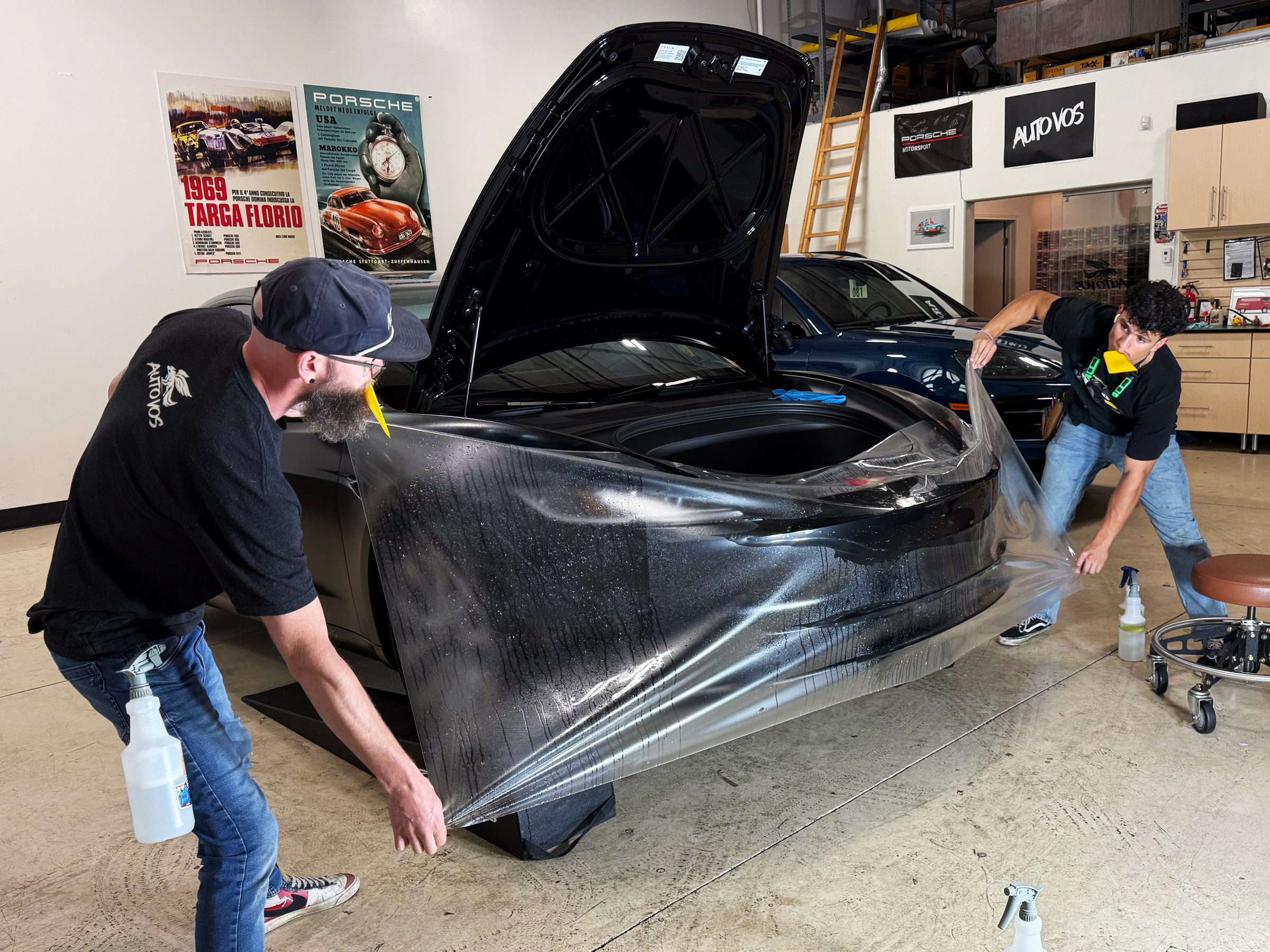 Two installers positioning clear paint protection film around a car’s front bumper Two installers positioning clear paint protection film around a car’s front bumper