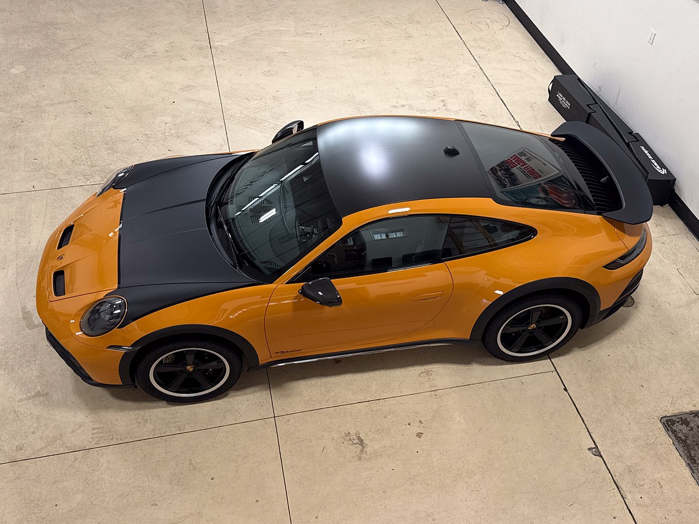 Overhead view of an orange Porsche 911 with a black hood, roof and rear wing at Auto Vos Overhead view of an orange Porsche 911 with a black hood, roof and rear wing at Auto Vos