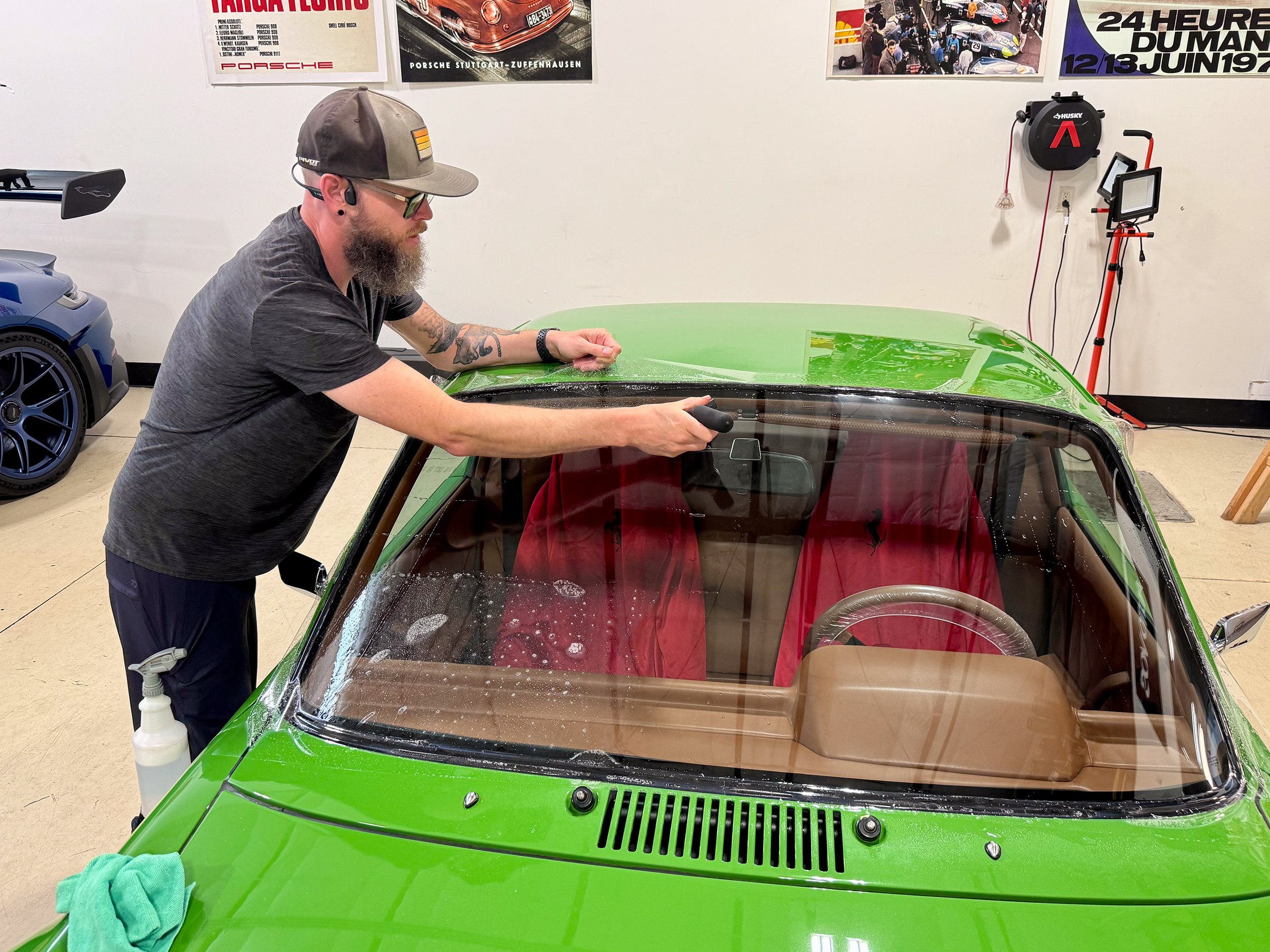 Installer fitting clear windshield protection film along the top edge of a green Porsche 914 Installer fitting clear windshield protection film along the top edge of a green Porsche 914